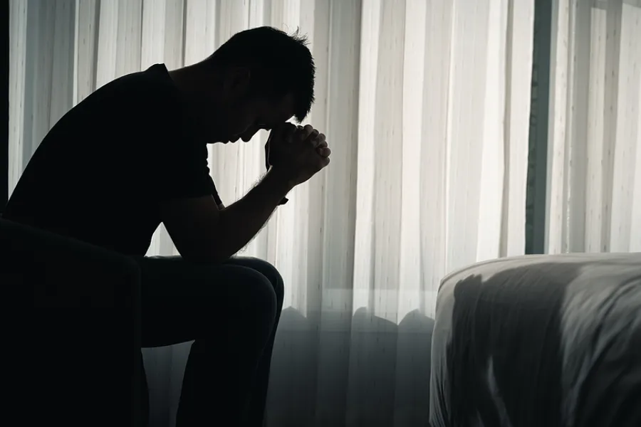 Silhouette of a man sitting with his head bowed and hands clasped