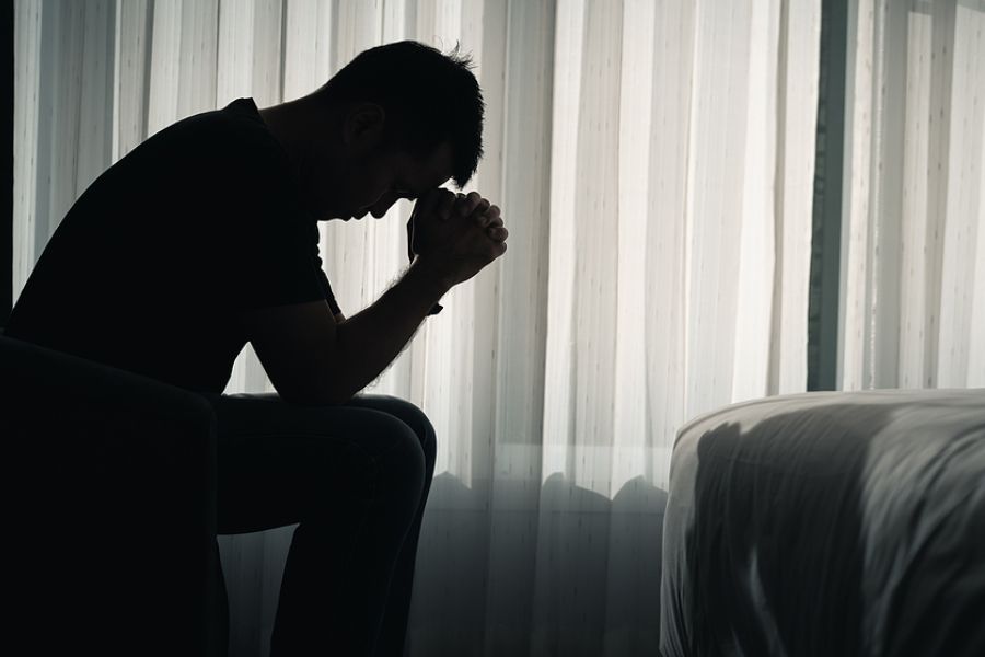 Silhouette of a man sitting with his head bowed and hands clasped