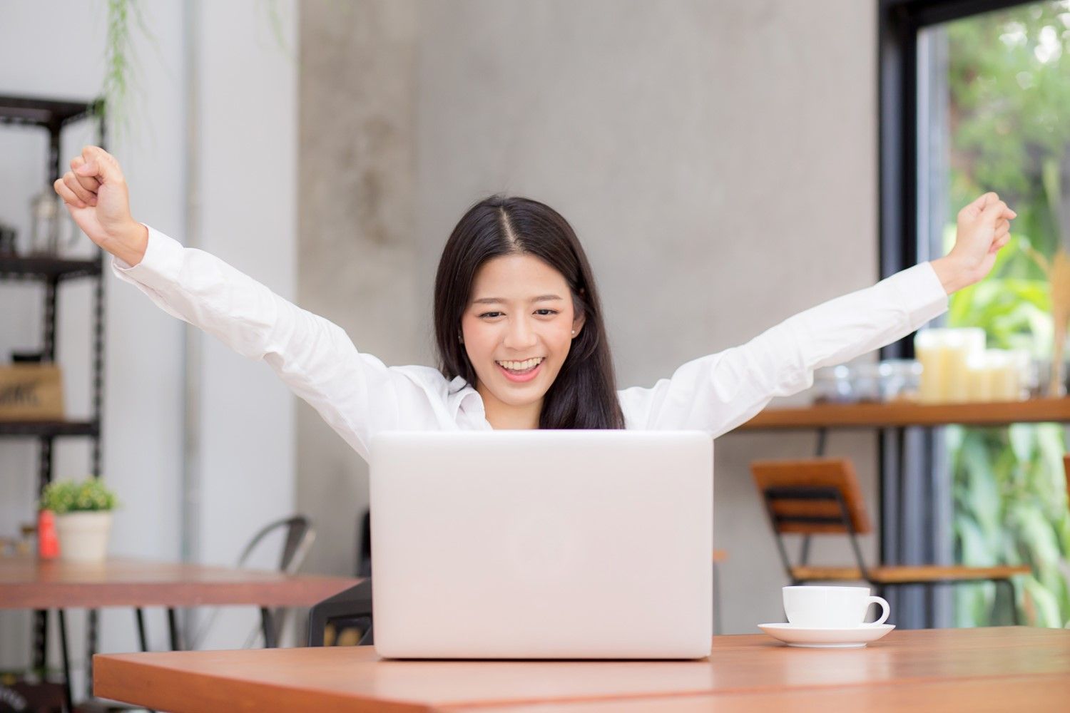 Smiling woman raising her arms while using a laptop