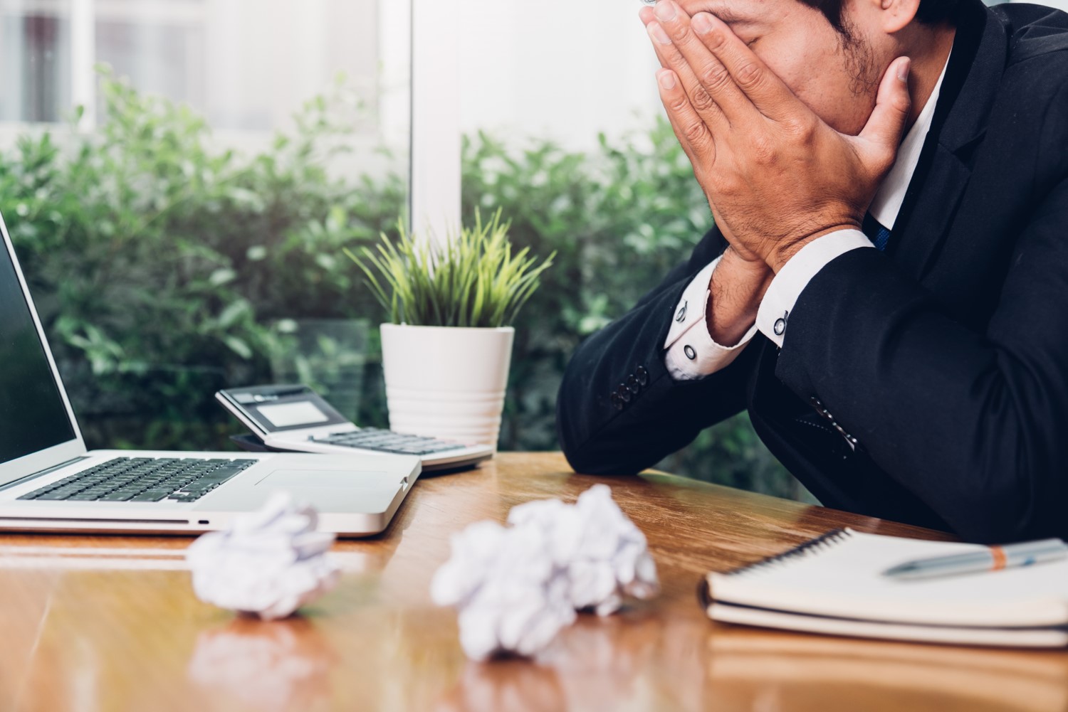 A man infront of laptop with many crushed papers stressed